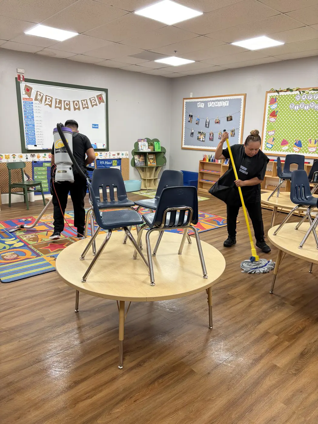 Two of our team vacuuming and mopping a classroom with chairs up on the tables